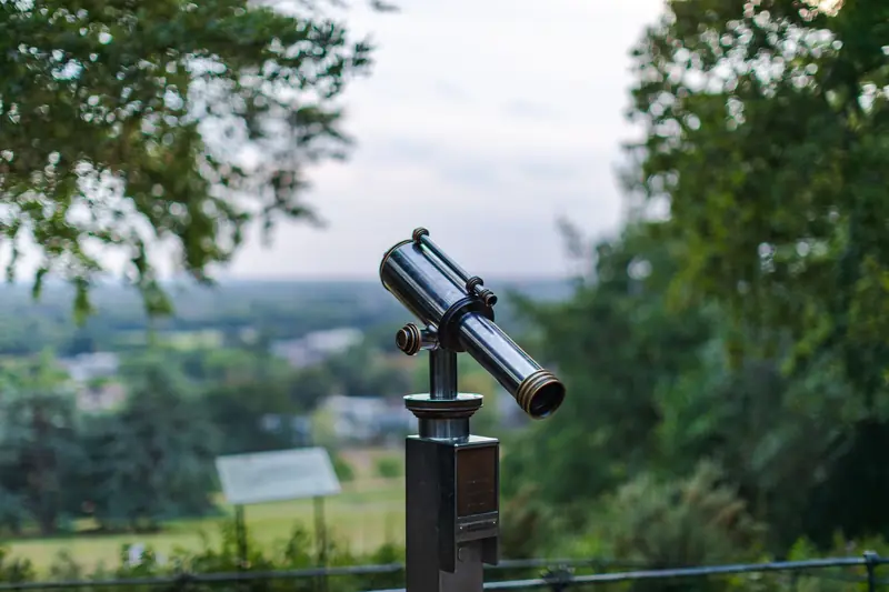 A public telescope pointing towards a scenic green landscape during the day