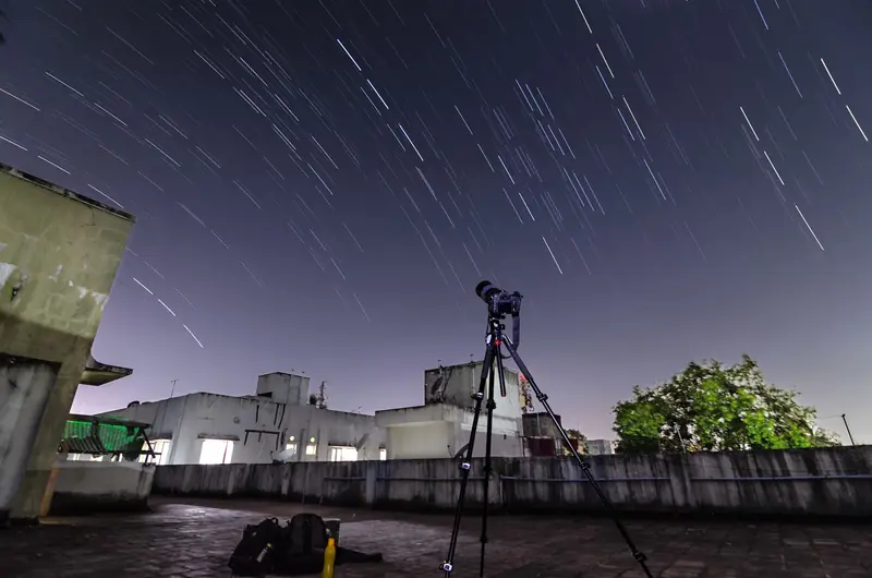A telescope on a rooftop captures star trails in the night sky