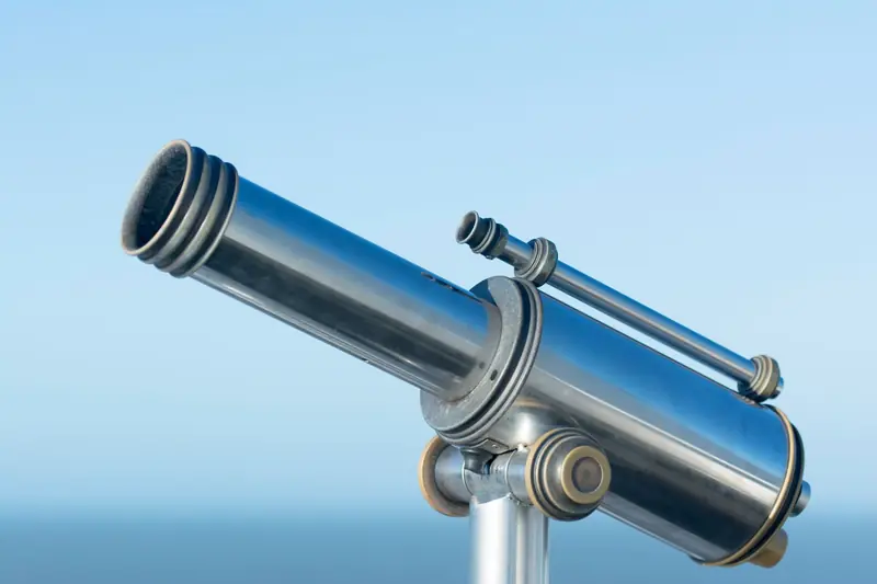 A sleek metallic coin-operated telescope pointing into a clear blue sky, perfect day for sightseeing