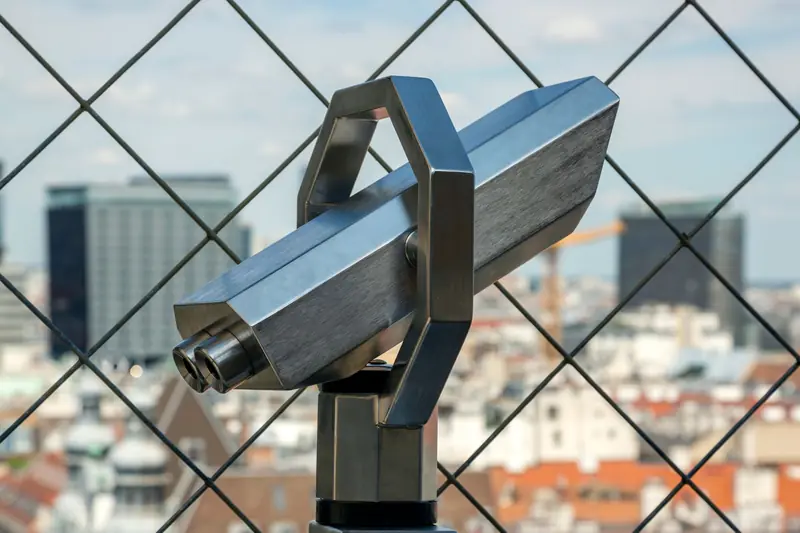 Fixed telescope with city skyline view through a grid fence, perfect for urban exploration visuals