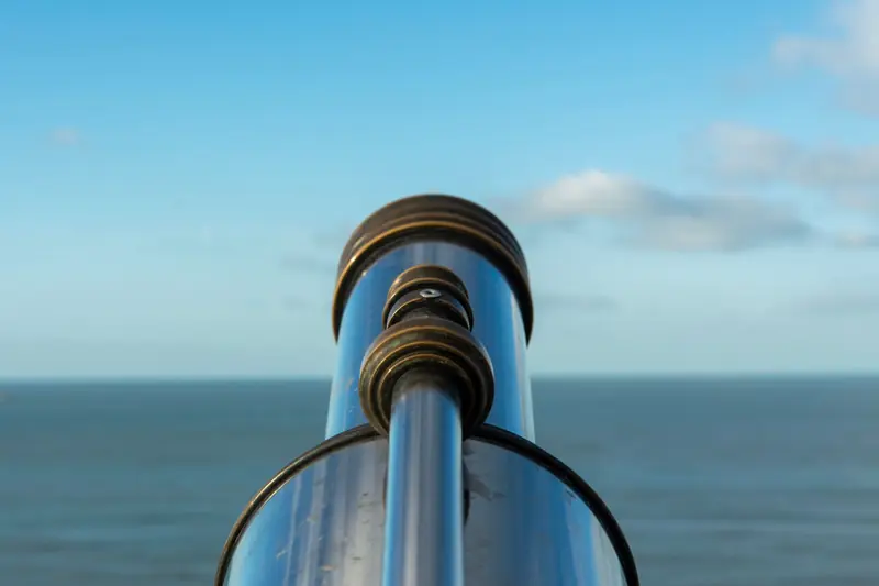 A shiny telescope facing a vast ocean under a clear blue sky, perfect for beachside observation