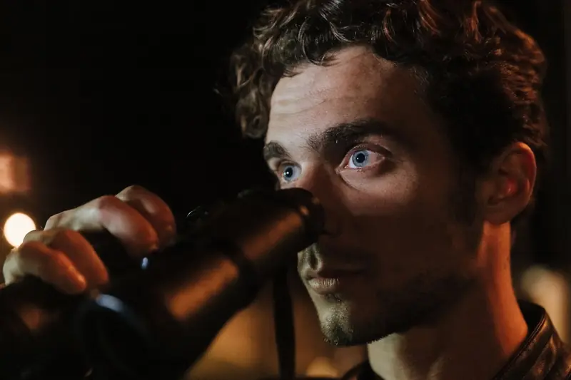 Close-up of a man with intense gaze using binoculars during night time observation