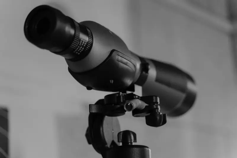 Detailed monochrome image of a modern telescope lens mounted on a tripod