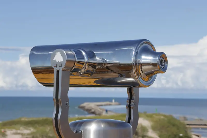 A shiny metallic telescope overlooks the ocean on a clear day, offering scenic views