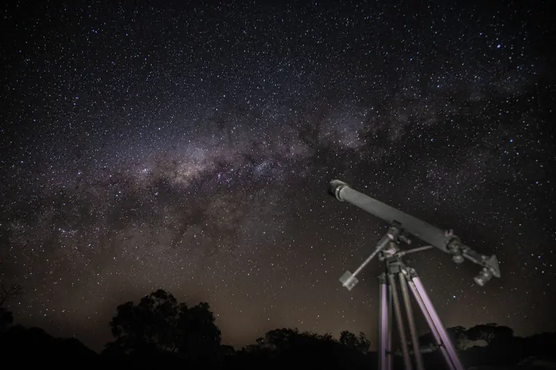 A telescope gazes at a stunning starry night sky showcasing the Milky Way